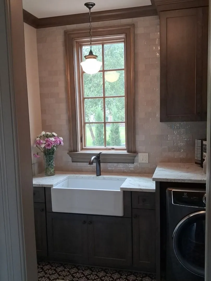 Warm white tile backsplash behind a farmhouse sink with dark cabinetry and a window