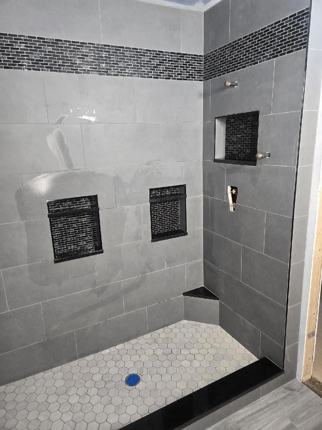Large-format gray shower tile with black mosaic niches and a hexagon floor